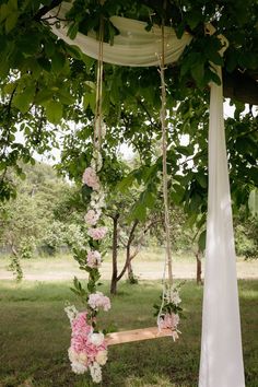 a wooden swing with flowers and greenery hanging from it's sides in the grass