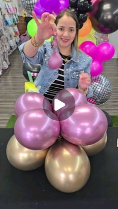 a woman standing in front of balloons and giving the peace sign with her hand while she is surrounded by other balloons