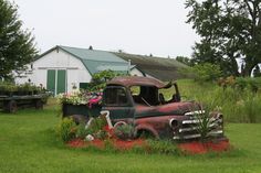 an old truck sitting in the middle of a field with flowers growing out of it