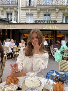 a woman covering her mouth while sitting at a table with food and drinks on it