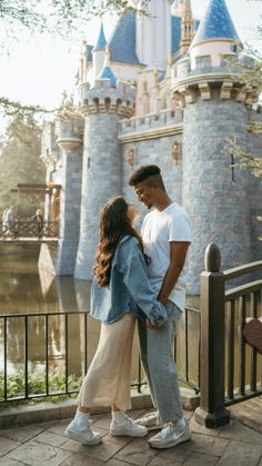 a man and woman standing next to each other in front of a castle at disneyland