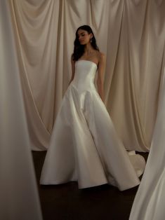 a woman in a white wedding dress standing next to curtains