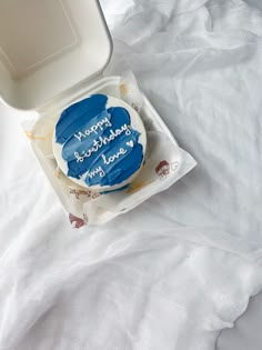 a blue frosted birthday cake sitting on top of a white plate in a box