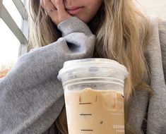 a woman sitting at a table with a cup of coffee in front of her face