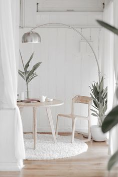 two chairs and a table in a white room with plants on the floor next to them