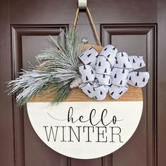 a welcome sign hanging on the front door with pine cones and evergreens in it