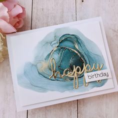 a card with the words happy birthday written in gold on it next to some flowers