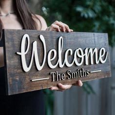 a woman holding a wooden sign that says welcome the smiths