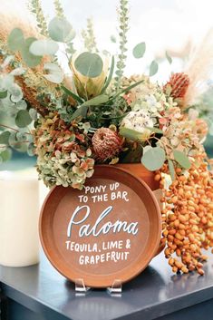 a vase filled with flowers and greenery on top of a table next to a candle