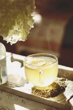 a cup of tea on a tray next to a vase with white flowers in it