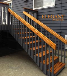 a wooden hand rail next to a gray house with wood steps on the front and side