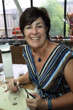 a woman sitting at a table with scissors in her hand and jewelry on the table