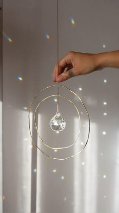 a hand holding a crystal ball hanging from a string in front of a white wall