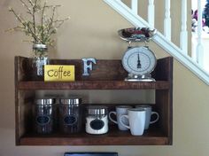 a shelf with coffee mugs and a clock on it next to a stair case