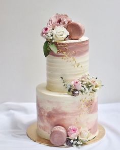 a three tiered cake with flowers and leaves on the top is decorated in white, pink and gold