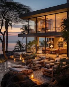 an outdoor living area with couches and candles on the ground next to water at dusk