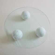 three marble balls sitting on top of a round glass table with white walls in the background