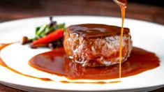 a piece of meat covered in gravy on a white plate next to a strawberry