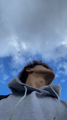 a man wearing a hoodie looking up into the sky with a bird flying overhead