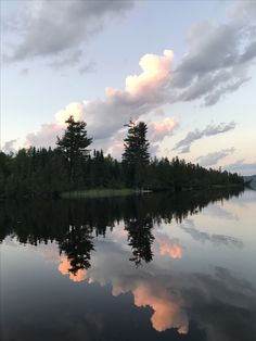 the clouds are reflected in the still water on the lake's surface as the sun sets