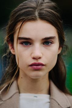 a woman with long hair and blue eyes looks at the camera while wearing a beige coat