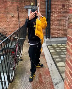 a person taking a selfie in front of a brick building with a bicycle parked on the sidewalk