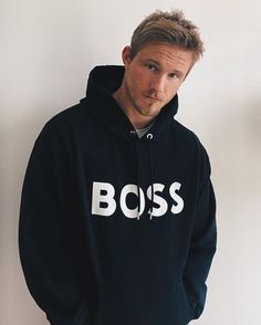 a man wearing a black boss hoodie standing against a wall