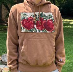 a man wearing a brown hoodie with two red hearts on it and green grass in the background