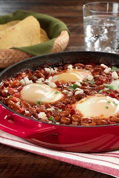 two eggs are in a red skillet on a table next to bread and water