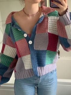 a woman taking a selfie in front of a mirror wearing a colorful sweater and jeans