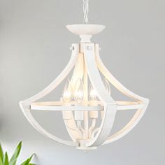 a white chandelier with three lights hanging from it's center and two plants in the background