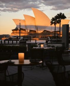 the sydney opera house is lit up at night with candles on tables and chairs around it