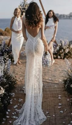 two women in white dresses walking down a path next to the ocean with flowers all around them