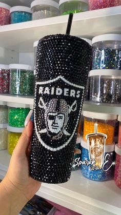 a person holding up a cup with the oakland football team on it in front of some glitters