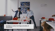 two men are standing in the middle of a room with desks and red chairs