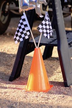 an orange cone with two flags sticking out of it sitting in the sand next to a black and white car