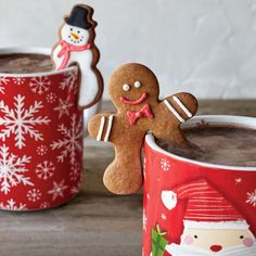 two mugs filled with hot chocolate and decorated gingerbread cookies, one in the shape of a snowman