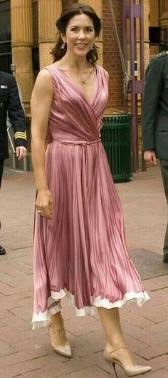 a woman in a pink dress is walking down the street with other people behind her