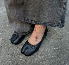 a woman's foot with a cross tattoo on her left ankle and black shoes