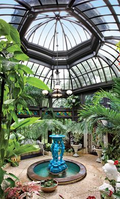 the inside of a glass house with plants and water fountain in the center, surrounded by greenery