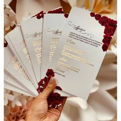 a person holding five cards with red roses on them in front of some white flowers