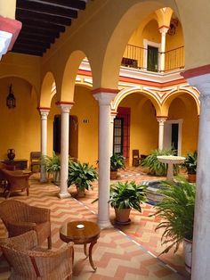 an indoor courtyard with potted plants and wicker chairs in the foreground, surrounded by arches