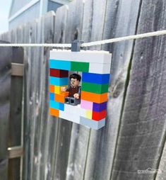 a lego photo hanging on a clothes line with a wooden fence in the back ground