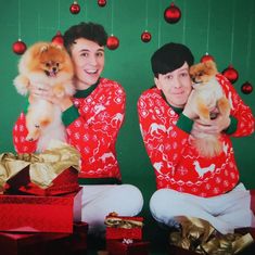 two young men holding small dogs in front of christmas decorations and presents on the floor