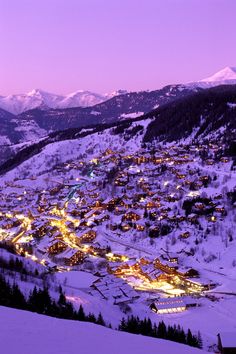 a town is lit up at night in the snowy mountains with snow on the ground