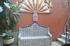 a bench sitting next to a potted plant in front of a wall with a fan on it