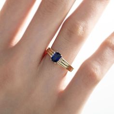 a woman's hand wearing a gold ring with an oval blue stone on it