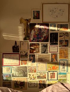 a wall covered in pictures and drawings next to a bed