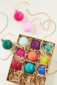 an open box filled with different colored eggs on top of a white table next to two necklaces