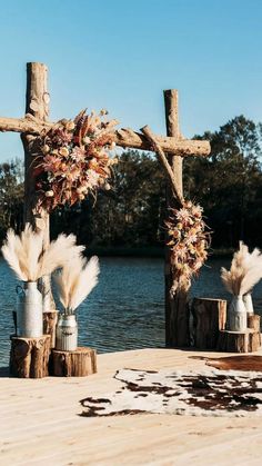 an outdoor wedding setup with flowers and candles on the dock by the water in front of a wooden cross